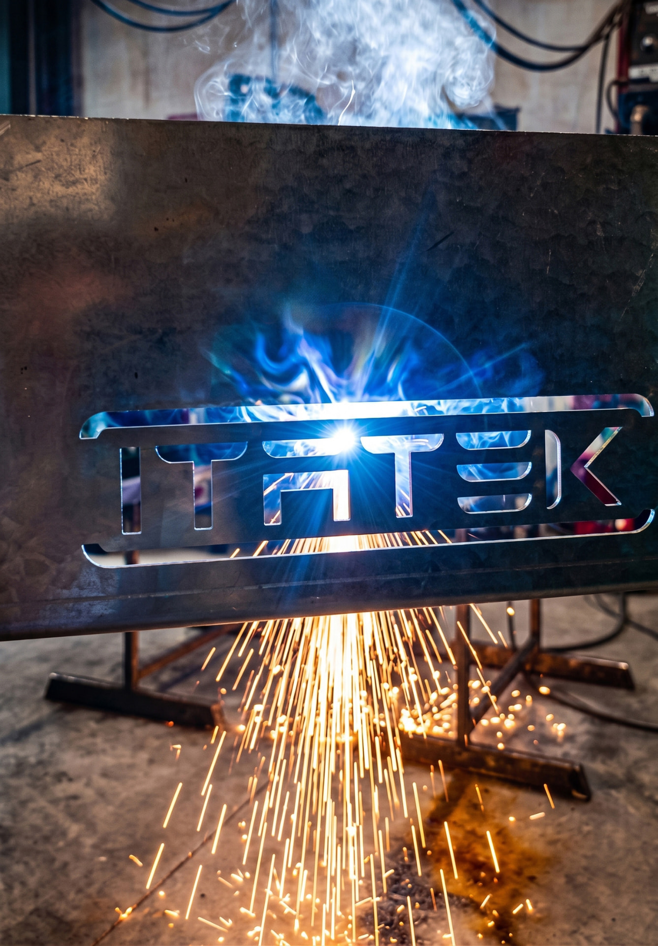 Arco di luce e scintille dietro una lastra di metallo con il marchio ITATEK tagliato al laser