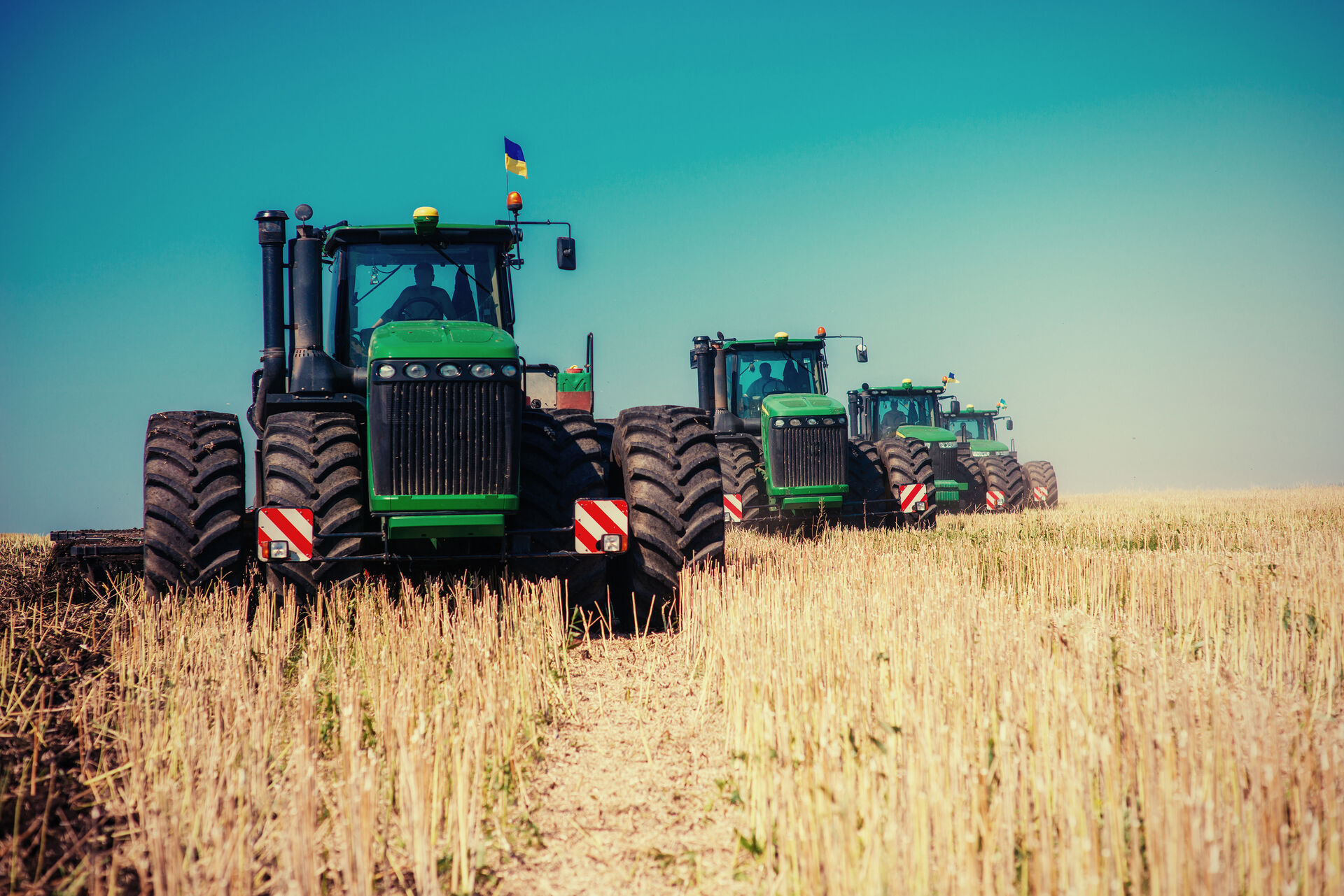 Trattori agricoli moderni al lavoro in un campo di grano al tramonto